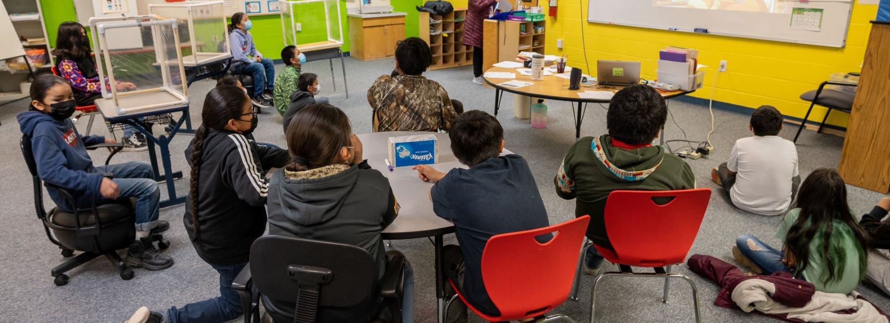Several students sitting in a classroom, attentively looking at the board.