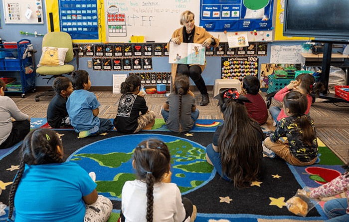 Teacher reading to a classroom of students who are sitting on the floor. 
